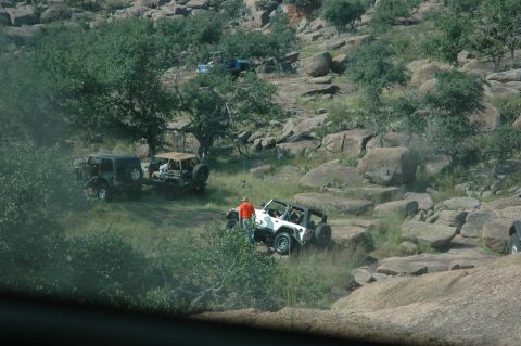 2001 Jeep Wrangler - Several Jeeps navigate a rocky, off-road terrain with trees and boulders scattered throughout the landscape.