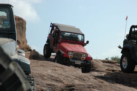 2001 Jeep Wrangler - A red Jeep Wrangler navigates a rocky incline, with another Jeep visible to the right and the front of a third Jeep on the left.