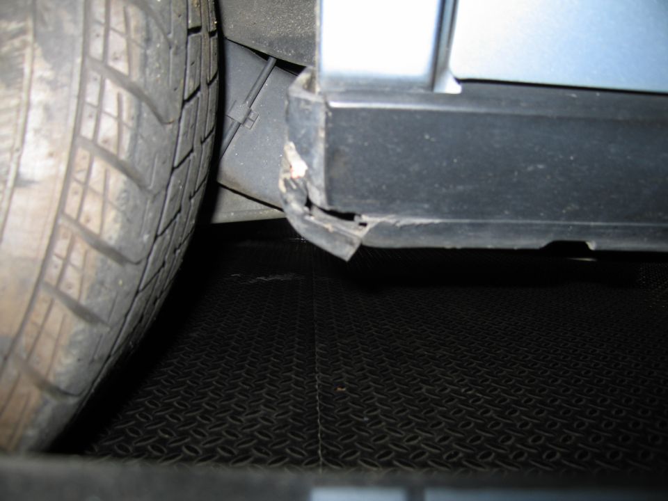 Close-up of a car's side panel and tire, showing damage to the black trim below the door