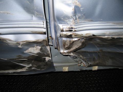 1991 Ford LTD Crown Victoria - The car's side paneling is severely dented and scraped, showing significant damage to the door and fender area.