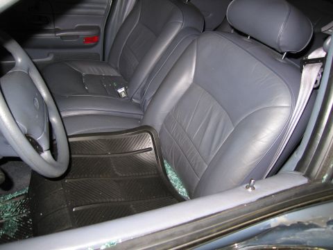 1991 Ford LTD Crown Victoria - The interior of a car shows gray leather seats and a steering wheel, with shattered glass scattered on the floor mat.
