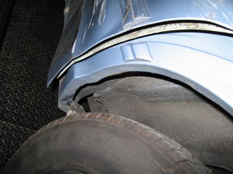 1991 Ford LTD Crown Victoria - Close-up view of the wheel well and fender of a blue vehicle, showing some damage to the bodywork.