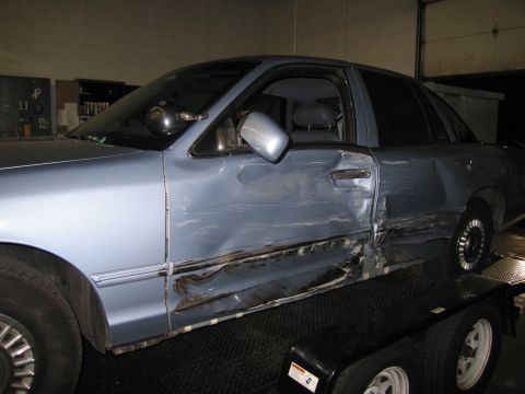 1991 Ford LTD Crown Victoria - The side of a blue sedan shows extensive damage to the door and rear fender area.