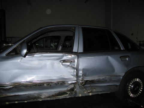 1991 Ford LTD Crown Victoria - Side view of a heavily damaged light blue sedan, showing significant impact on the front and rear doors.