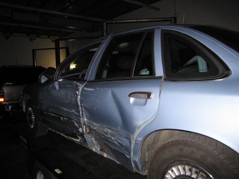 1991 Ford LTD Crown Victoria - A blue sedan shows extensive damage to its driver's side, with another vehicle visible in the background.
