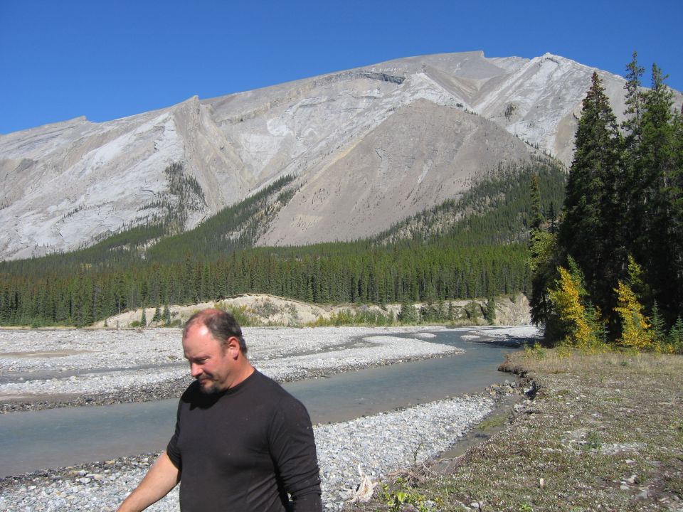 Man by a river with mountains and trees in the background
