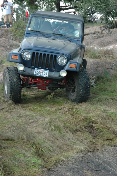 2001 Jeep Wrangler - A blue Jeep Wrangler navigates a rocky, grassy incline during an off-road excursion.