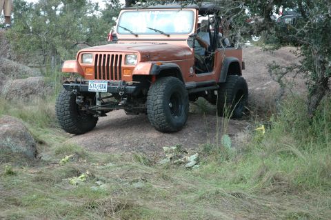 2001 Jeep Wrangler - An orange Jeep Wrangler navigates a rocky terrain, with another vehicle visible in the background.