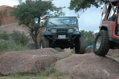 2001 Jeep Wrangler - Two Jeeps navigate rocky terrain, with the green Jeep Wrangler in the foreground showing its front end and off-road modifications.