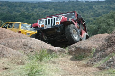 2001 Jeep Wrangler - A red 2001 Jeep Wrangler navigates a rocky off-road course, with a yellow Jeep visible in the background.