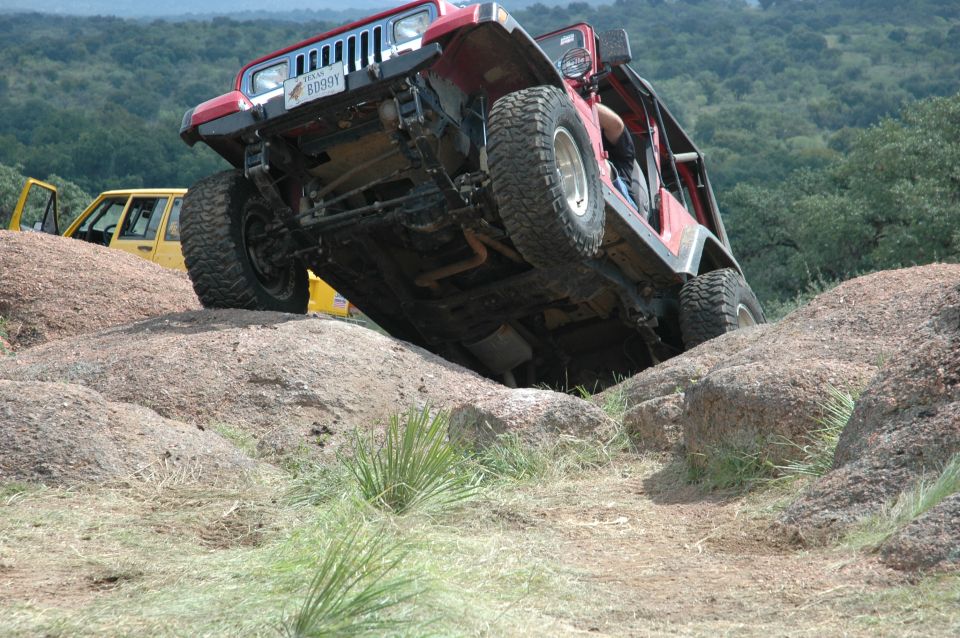 Red 2001 Jeep Wrangler climbing over large rocks, yellow Jeep in background