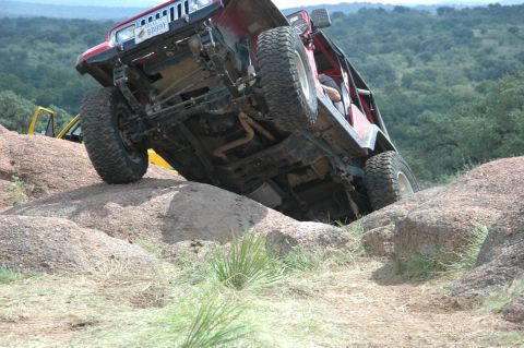 2001 Jeep Wrangler - This red Jeep is navigating a rocky trail, showing its undercarriage and suspension.