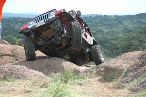 2001 Jeep Wrangler - A red Jeep Wrangler navigates a rocky terrain, showing its undercarriage.