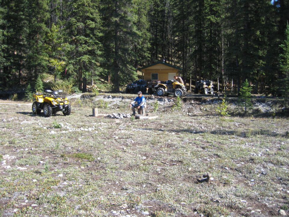 Yellow ATV parked in a campsite scene with a cabin and other ATVs