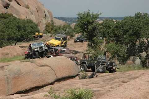 2001 Jeep Wrangler - A group of Jeeps navigate a , rocky landscape with trees and distant hills.