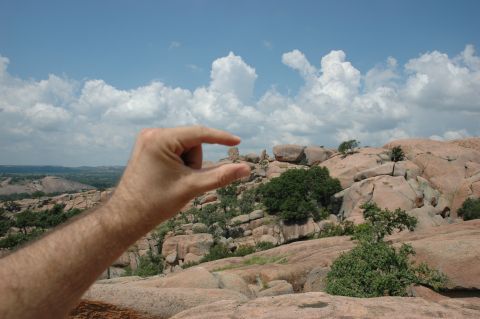 2001 Jeep Wrangler - A hand appears to pinch a distant rock formation in a vast, arid landscape under a partly cloudy sky.