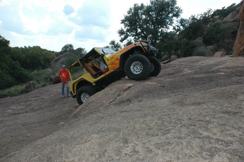 2001 Jeep Wrangler - A yellow 2001 Jeep Wrangler navigates a steep, rocky incline with a person standing nearby.