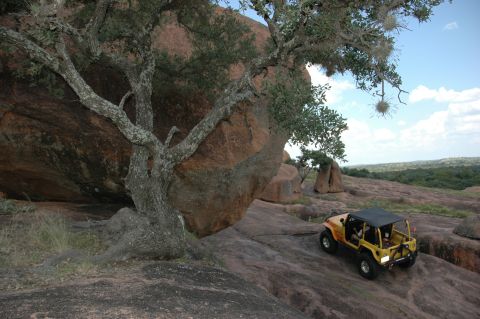 2001 Jeep Wrangler - Yellow 2001 Jeep Wrangler navigating a rocky landscape with large boulders and trees.