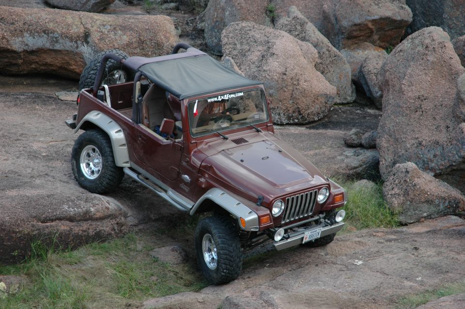 Maroon Jeep Wrangler on rocks, has a www.4x4fun.com sticker on windshield