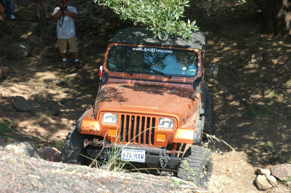 Orange Jeep Wrangler going downhill on a rocky trail. Has a "www.4x4fun.com" sticker on the windshield