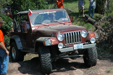 2001 Jeep Wrangler - A maroon 2001 Jeep Wrangler navigates a rocky terrain, with onlookers present.