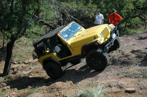 2001 Jeep Wrangler - A yellow 2001 Jeep Wrangler navigates a challenging off-road trail with steep inclines and loose rocks.
