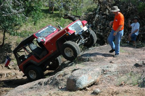2001 Jeep Wrangler - Red Jeep Wrangler navigating a steep, rocky incline with two onlookers observing.