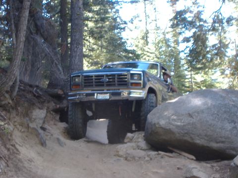 1986 Ford Bronco - This lifted Ford Bronco is shown off-roading on a dirt path with large rocks.