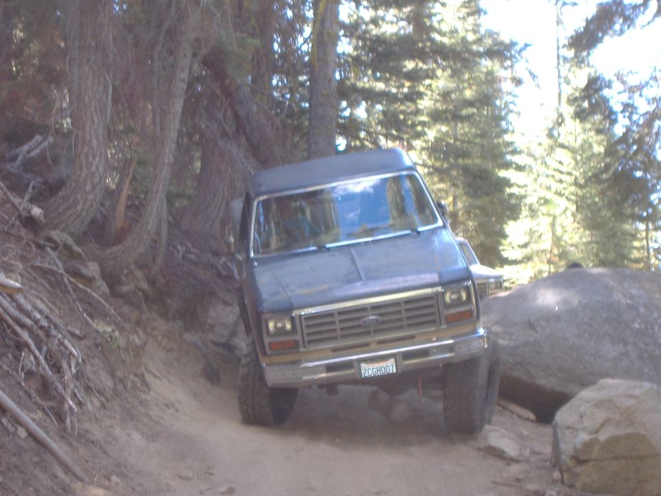 Dark blue SUV with a chrome grille and a license plate reading 'PCCGH001' driving on a dirt road
