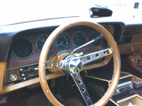 1979 Ford Ranchero - The interior of a 1979 Ford Ranchero features a wood-grain dashboard and an aftermarket steering wheel with a chrome horn button.