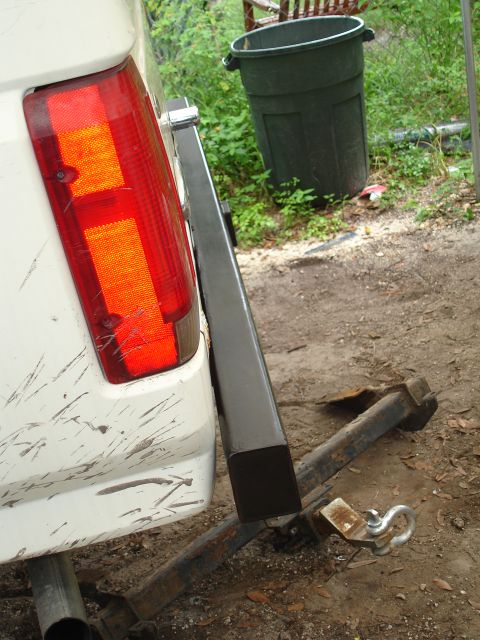 1989 Ford Bronco - The rear of a white vehicle is visible, a cracked taillight and a trailer hitch. A large trash can is in the background.
