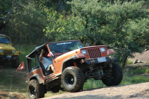 2001 Jeep Wrangler - An orange Jeep Wrangler navigates a challenging off-road trail, with another Jeep visible behind it.