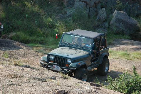 2001 Jeep Wrangler - A green Jeep Wrangler navigates a rocky, off-road trail, with another vehicle partially visible in the background.