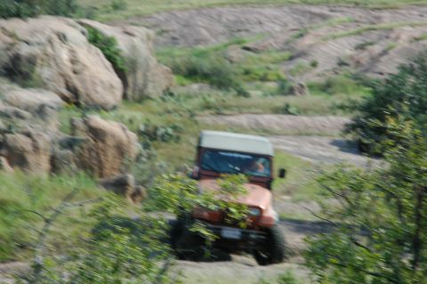 2001 Jeep Wrangler - An orange Jeep Wrangler navigates a , off-road terrain with another vehicle visible in the background.