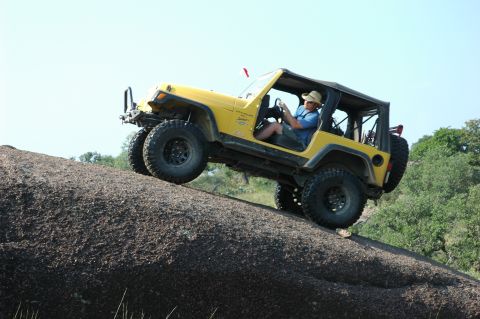 2001 Jeep Wrangler - Driver navigates a yellow Jeep Wrangler up a large rock formation on a clear day.