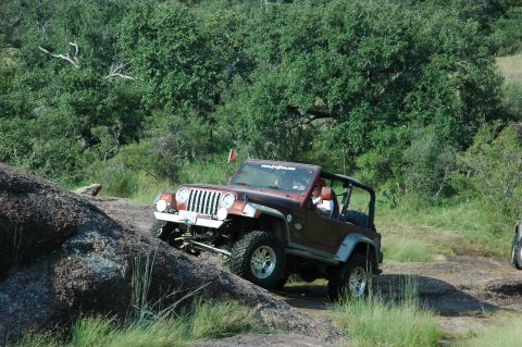 2001 Jeep Wrangler - A brown 2001 Jeep Wrangler navigates a rocky incline, its off-road capabilities. A partial view of another vehicle is visible to the right.