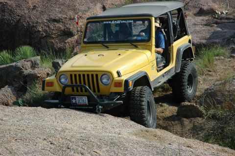 2001 Jeep Wrangler - A yellow Jeep Wrangler navigates a rocky trail, with a driver visible inside.