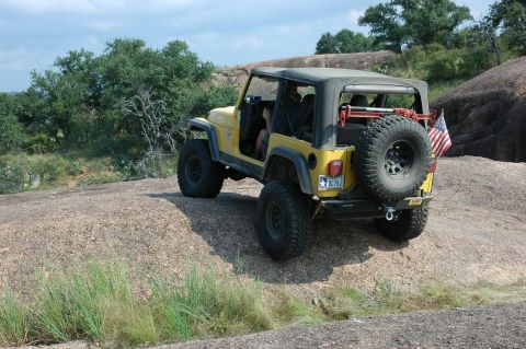 2001 Jeep Wrangler - A yellow 2001 Jeep Wrangler is parked on a rocky surface with trees in the background.