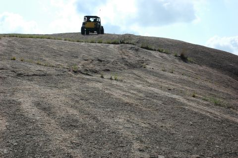 2001 Jeep Wrangler - A yellow Jeep ascends a large, rocky incline on a bright, cloudy day.