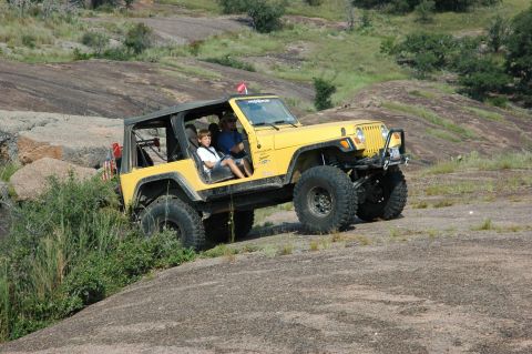 2001 Jeep Wrangler - A yellow 2001 Jeep Wrangler navigates a rocky incline, with two occupants visible inside.