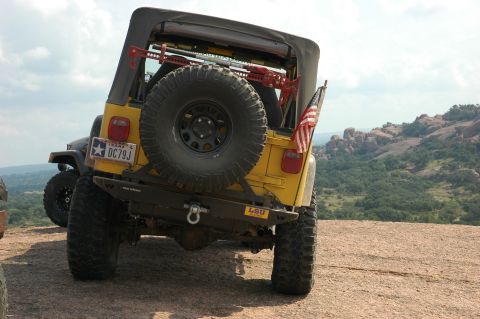 2001 Jeep Wrangler - Rear view of a yellow 2001 Jeep Wrangler parked on a rocky overlook with a scenic landscape.