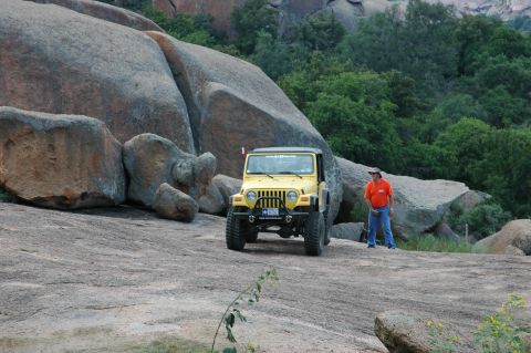2001 Jeep Wrangler - A yellow Jeep Wrangler is parked on a rocky surface, with a man standing beside it in an outdoor, natural setting.