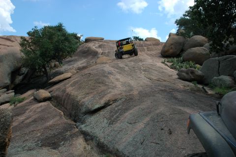 2001 Jeep Wrangler - A yellow 2001 Jeep Wrangler navigates a steep, rocky incline under a partly cloudy sky.