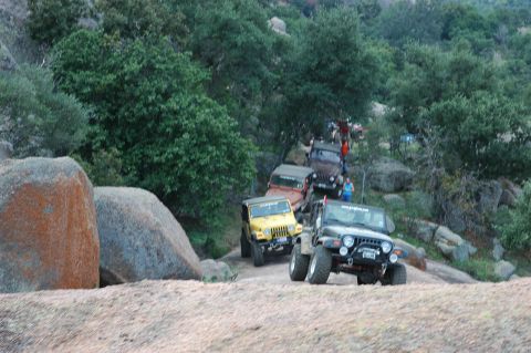2001 Jeep Wrangler - A group of Jeeps navigates a challenging off-road trail surrounded by natural rock formations and dense foliage.