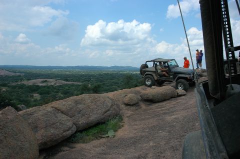 2001 Jeep Wrangler - A 2001 Jeep Wrangler navigates a rocky trail under a partly cloudy sky, with other vehicles and people nearby.