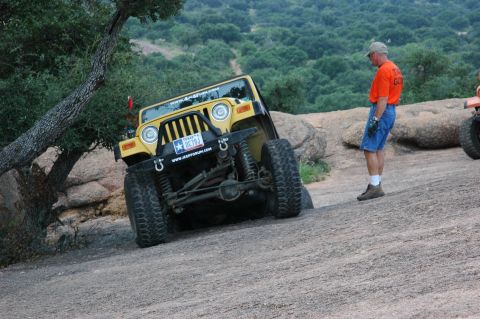 2001 Jeep Wrangler - A yellow 2001 Jeep Wrangler navigates a steep, rocky trail, with a man observing the off-road action.