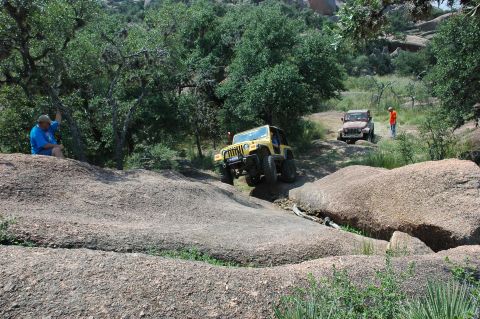2001 Jeep Wrangler - Two Jeeps navigate a challenging rocky trail with trees and boulders surrounding them.