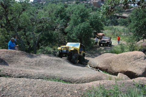 2001 Jeep Wrangler - Several Jeeps navigate a challenging off-road course amidst a rocky, wooded landscape.