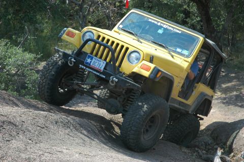 2001 Jeep Wrangler - Yellow 2001 Jeep Wrangler navigates a rocky trail with its tires angled on the terrain.
