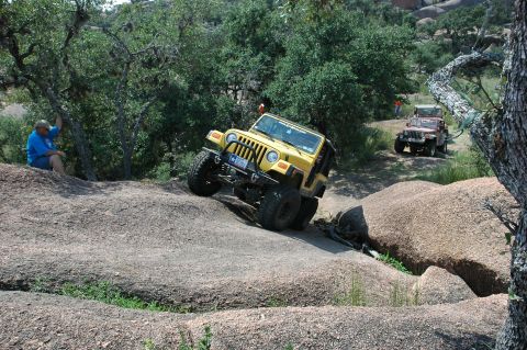 2001 Jeep Wrangler - Two Jeeps navigate a challenging off-road course with large rock formations and trees.